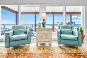 A room with two light blue armchairs, a white chest of drawers, a patterned rug, and a view of the ocean through large windows. - Getaway Beach Front, St. George Island Private 4  Bedroom Home (St. George Island)