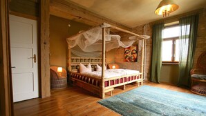 A four-poster bed with a canopy, a wicker chair, a green sofa, and a wooden floor. - Übersee - quiet guest apartment with terrace & clay plaster in Himmelpfort (Fürstenberg/Havel)