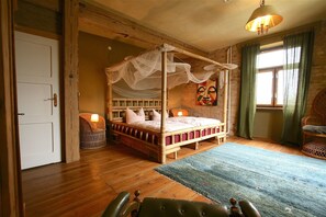 A four-poster bed with a canopy, a wicker chair, a green sofa, and a wooden floor.