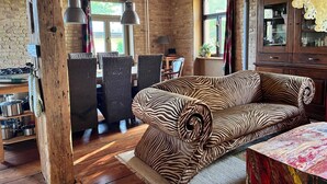 A rustic room with a zebra-patterned sofa, wooden beams, a dining area with chairs, and a kitchen with pots and pans. - Übersee - quiet guest apartment with terrace & clay plaster in Himmelpfort (Fürstenberg/Havel)