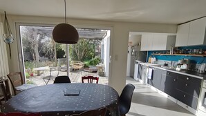 Eine moderne Küche mit weißen Schränken, einem Essbereich mit rundem Tisch und Stühlen sowie Blick auf den Garten durch die offene Tür.