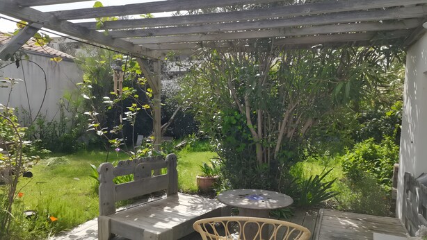 Eine Holzterrasse mit Bank und Korbsessel, umgeben von Grünpflanzen und einer Pergola.