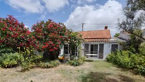 Ein Haus mit rotem Ziegeldach, ein Garten mit verschiedenen Pflanzen und ein weißes Tisch- und Stuhlgarnitur im Hof.