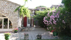 A stone building with a red door, a small patio with a table and chairs, and potted plants. - Rent house very beautiful mas provençal south Luberon - 10 beds (Mérindol)