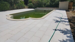A swimming pool with a tiled deck, surrounded by greenery and a building in the background. - Rent house very beautiful mas provençal south Luberon - 10 beds (Mérindol)