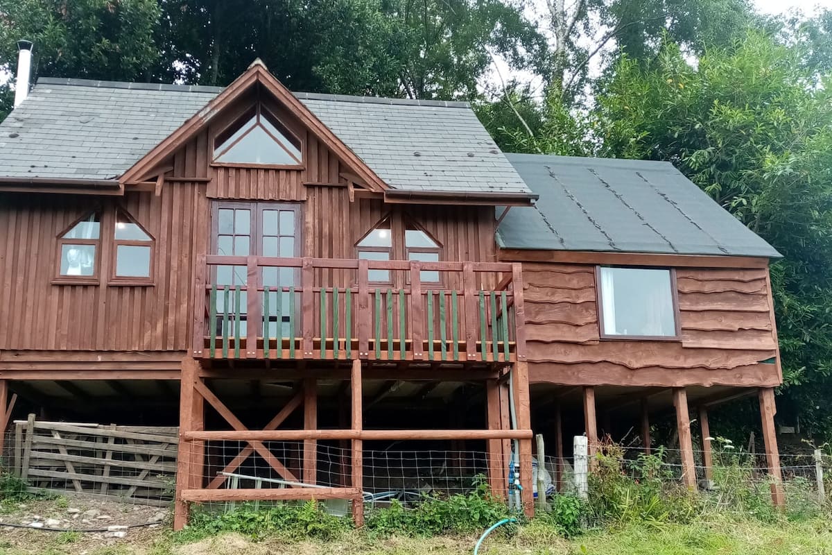A wooden cabin with a balcony, a chimney, and a fenced yard.