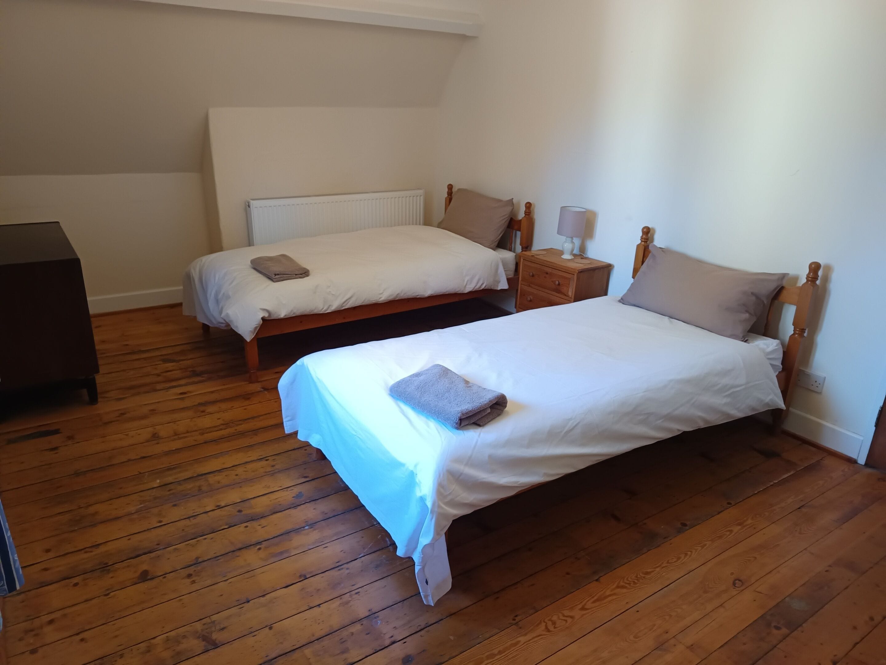 A room with two single beds, a wooden dresser, and a nightstand with a lamp.