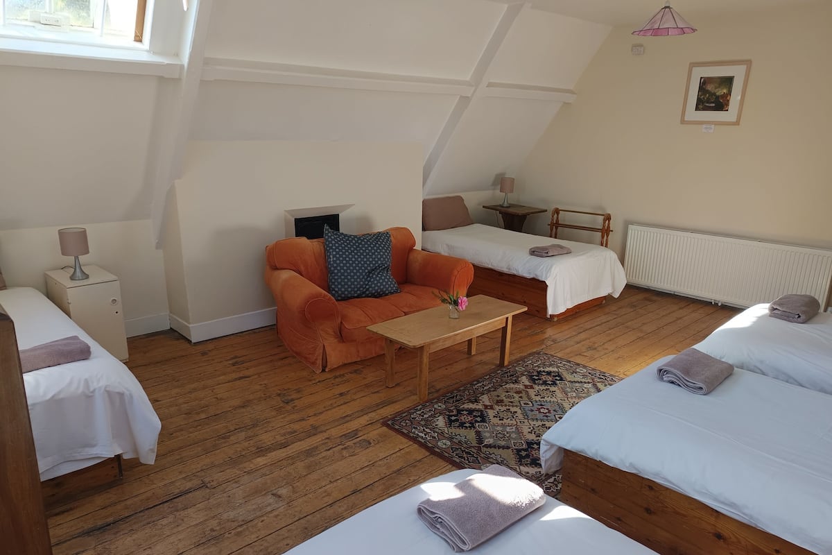 A cozy room with a sofa, two single beds, a small table, a lamp, and a radiator.