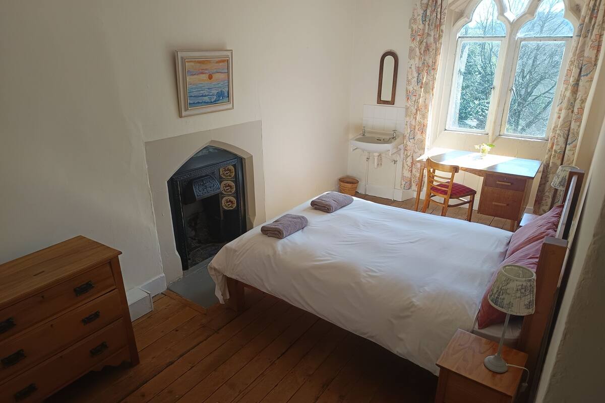 A bedroom with a bed, wooden dresser, desk, and a fireplace.