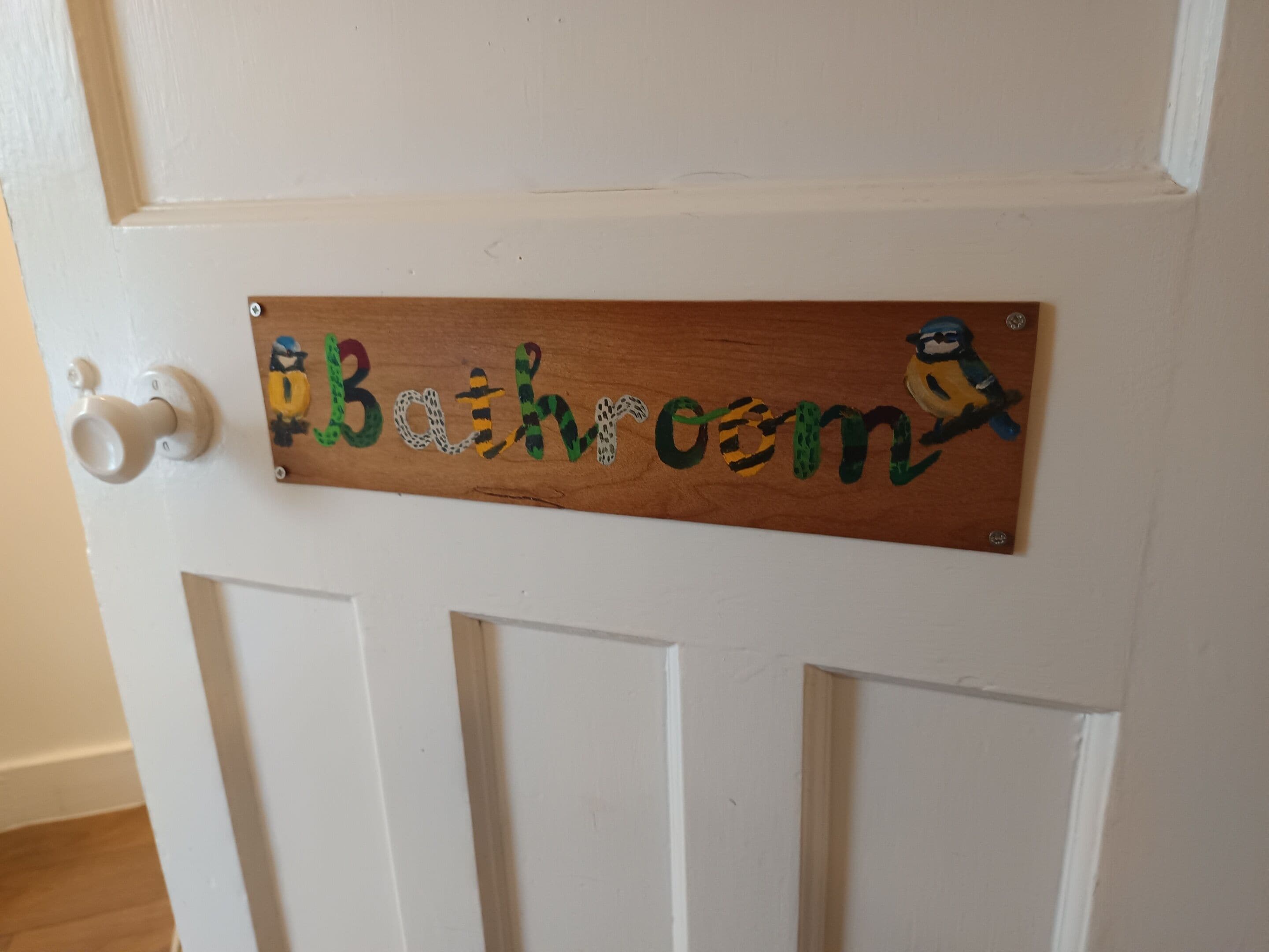 A wooden sign with the word 'Bathroom' and a cartoon character on a white door.