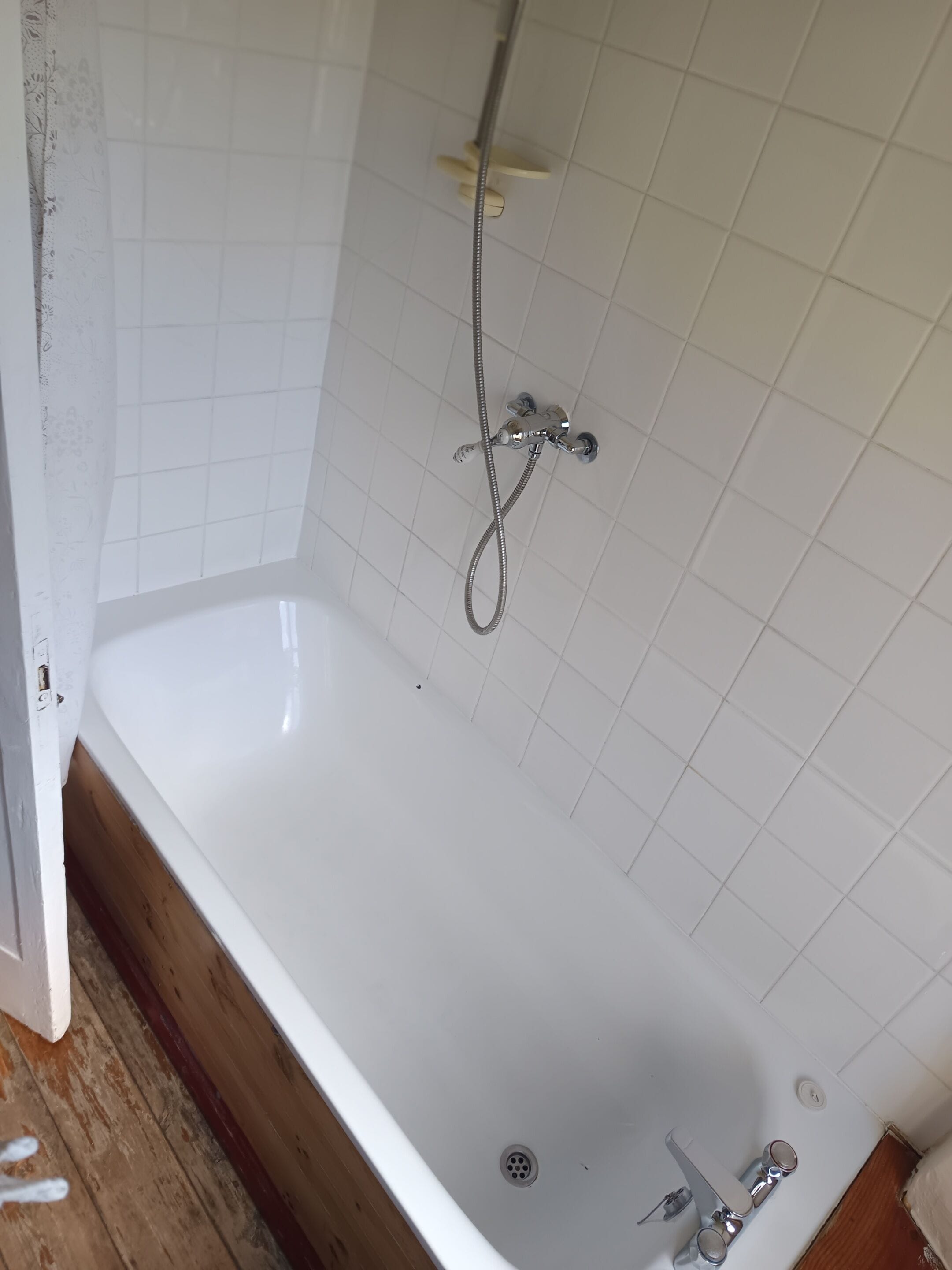 A bathroom with a white bathtub, a showerhead, and a tiled wall.