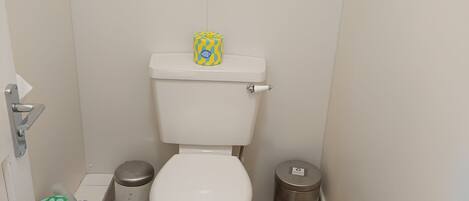 A small bathroom with a white toilet, a trash bin, and a bidet.