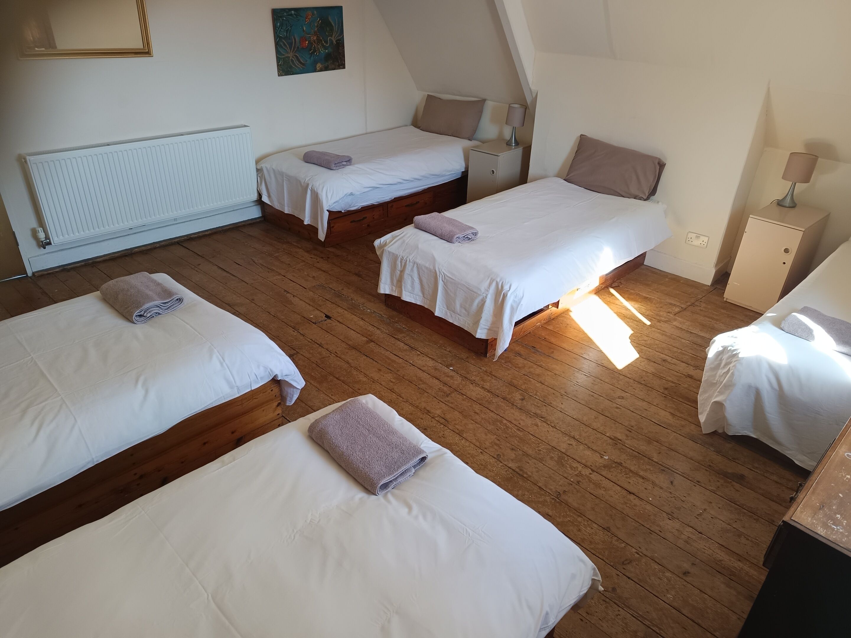 A room with four beds, a radiator, a painting, and a lamp.