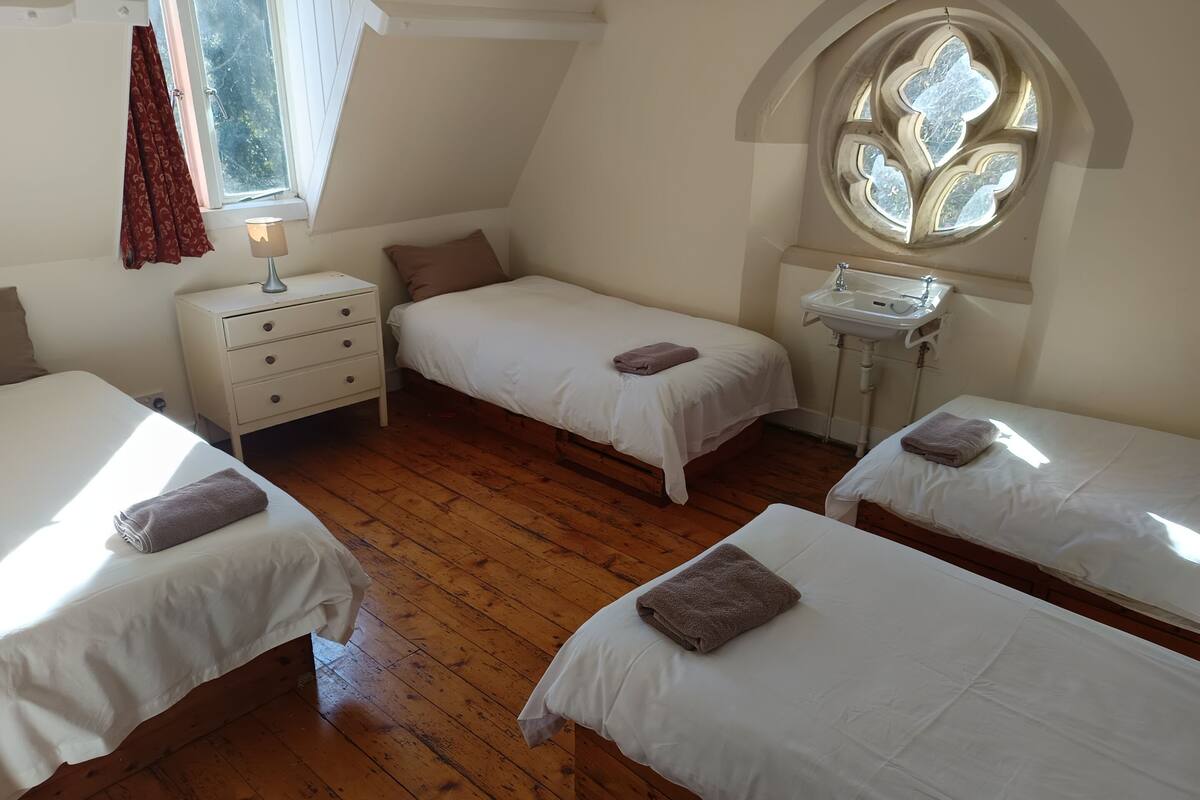 A room with three beds, a small white dresser, a window with a decorative design, and a sink.