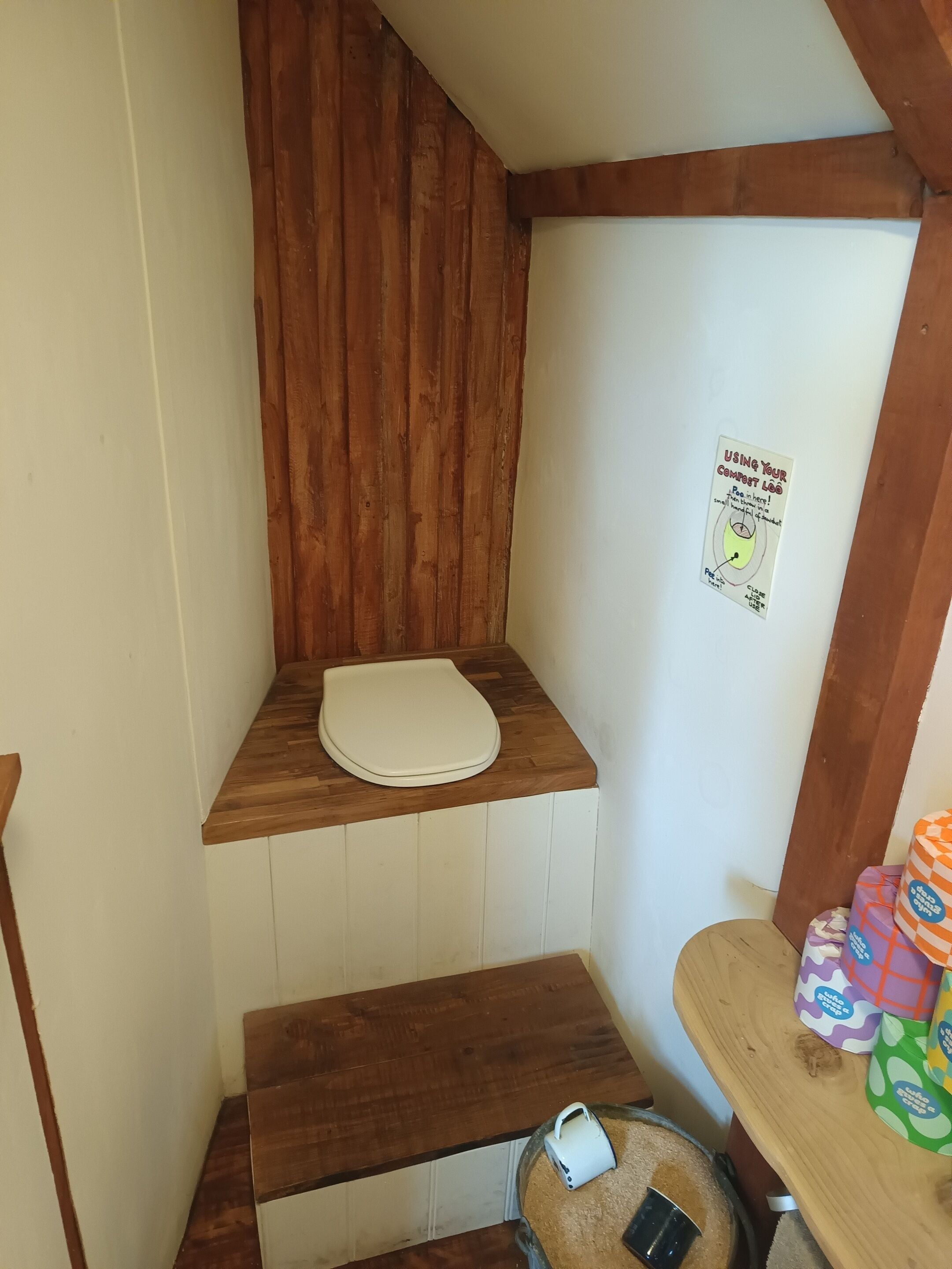 A small bathroom with a wooden bench, a toilet, and a sign instructing to use the commode.