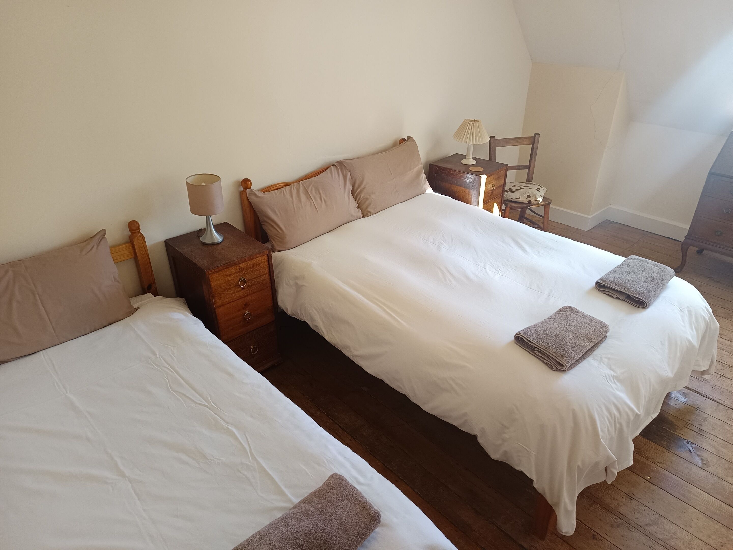 A bedroom with two beds, wooden headboards, a nightstand with a lamp, and a small table with a lamp.