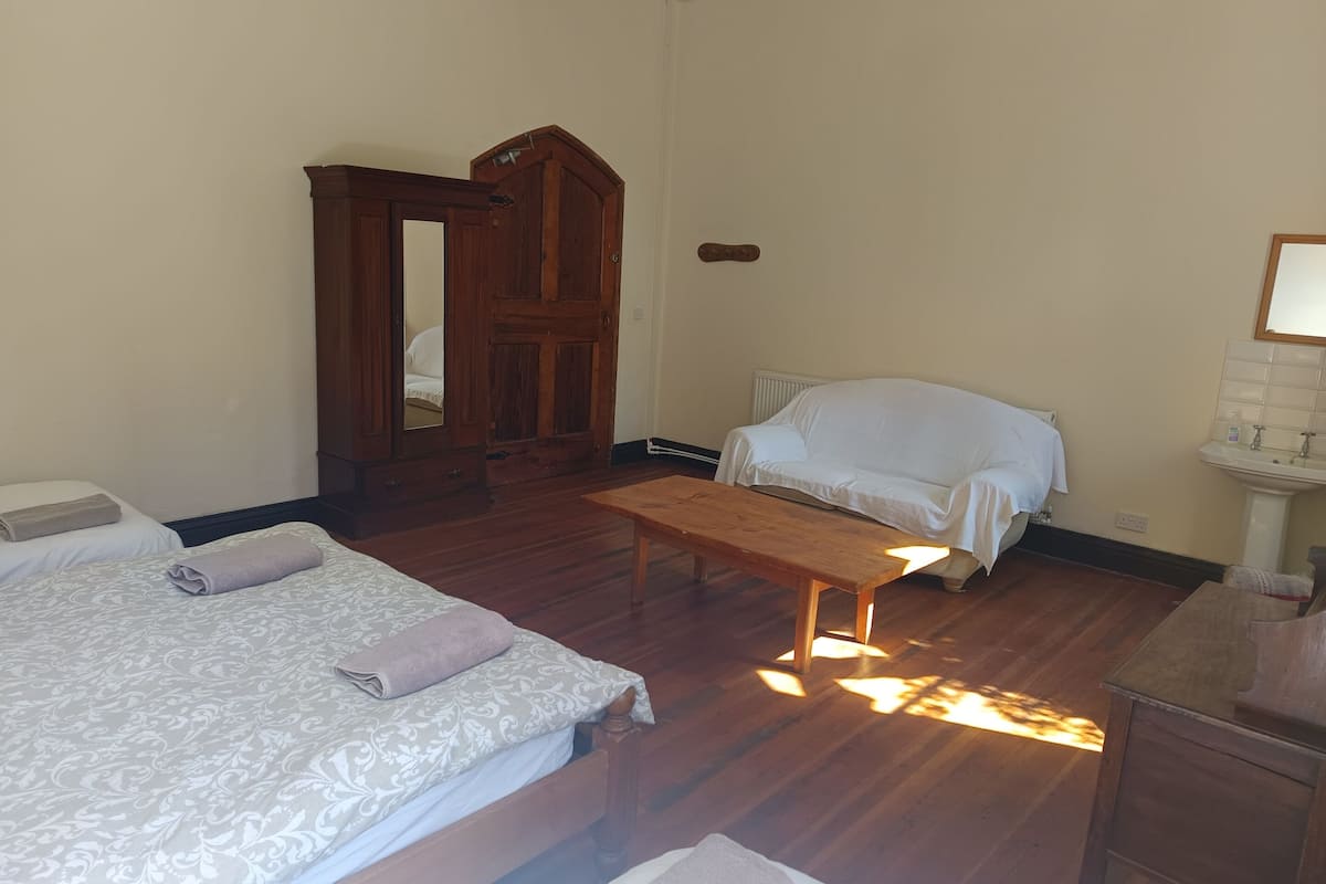 A room with two beds, a wooden bench, a white sofa, a wooden wardrobe, and a radiator.