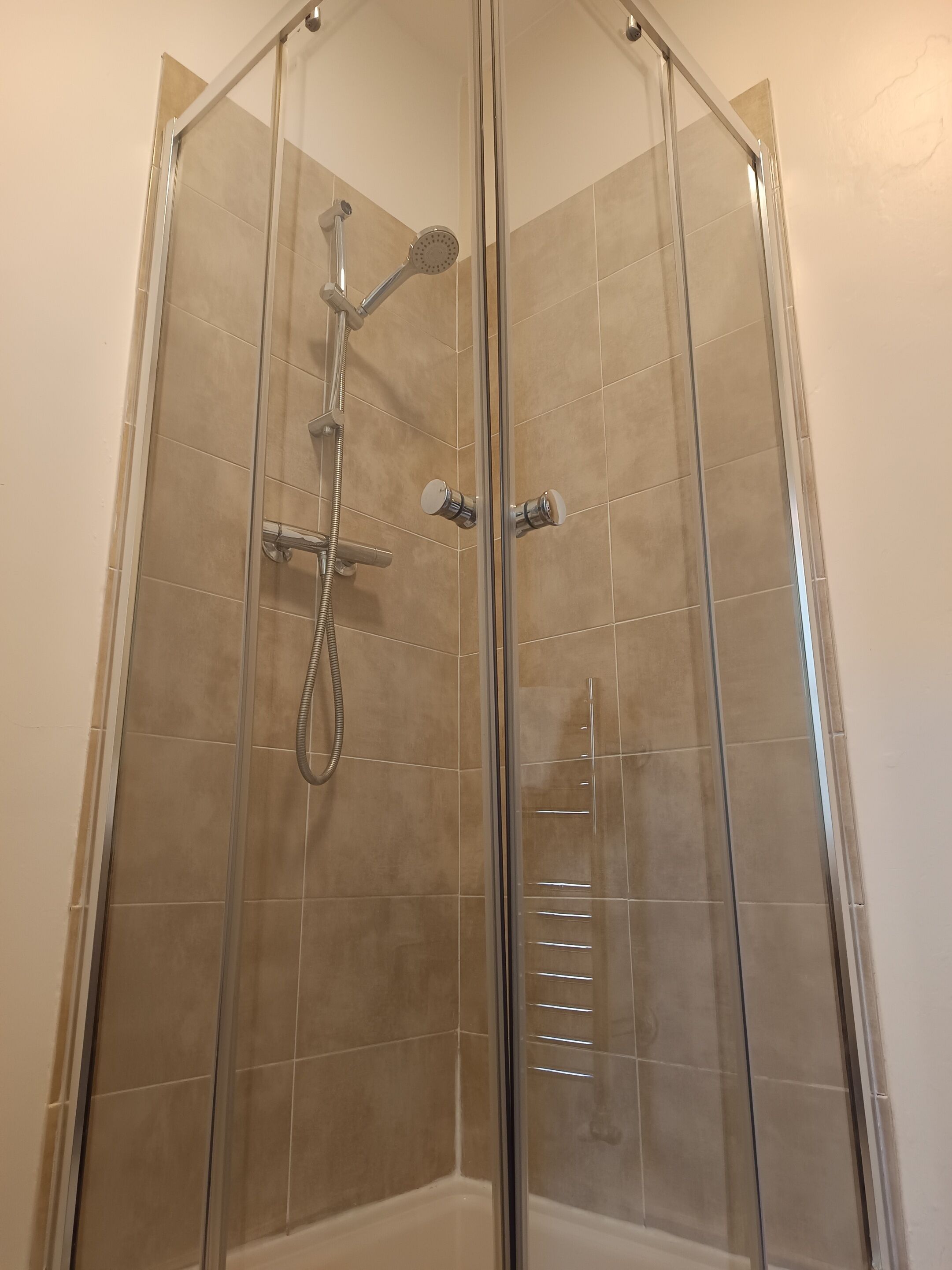 A glass-enclosed shower stall with a handheld showerhead and a wall-mounted faucet.