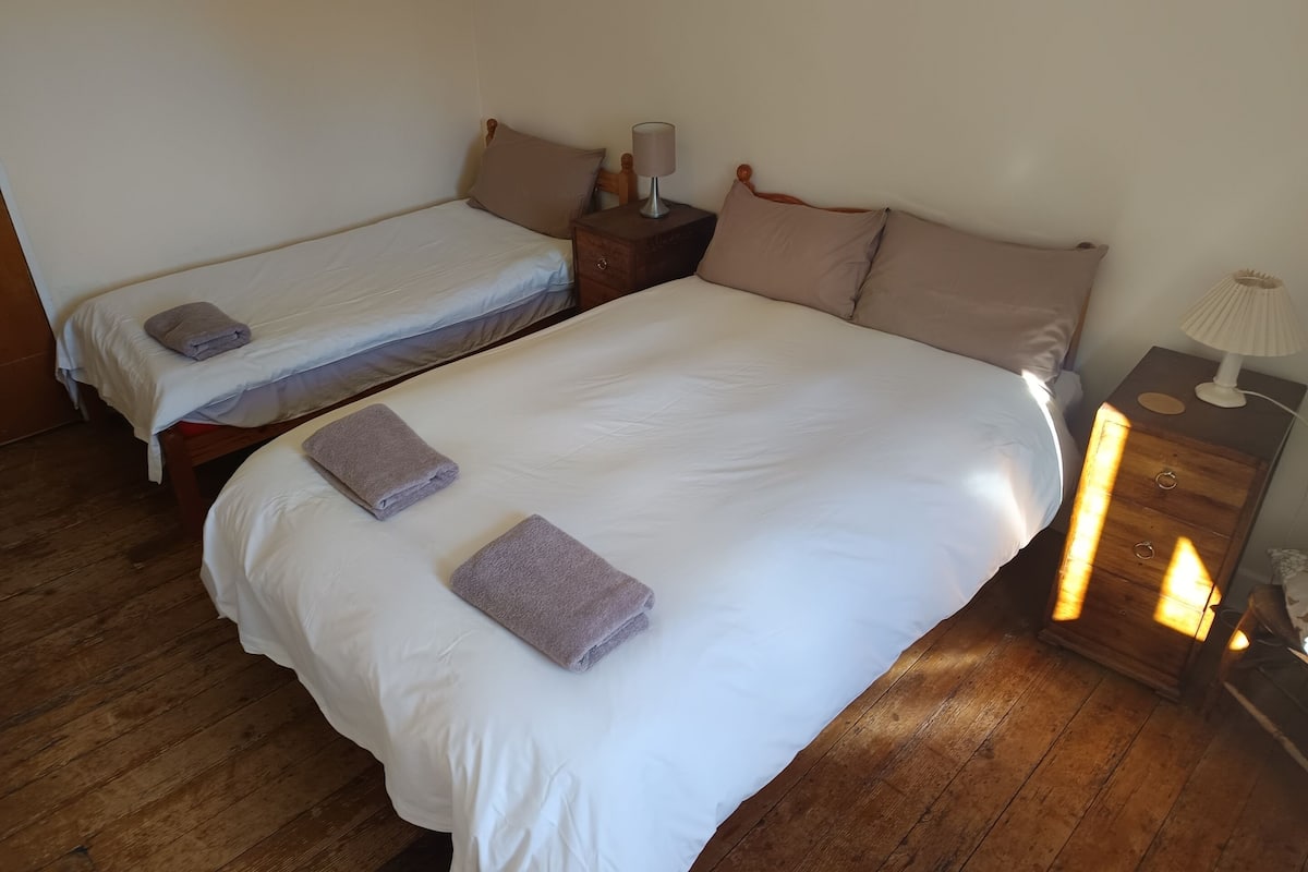 A room with two single beds, a wooden nightstand with a lamp, and a wooden floor.