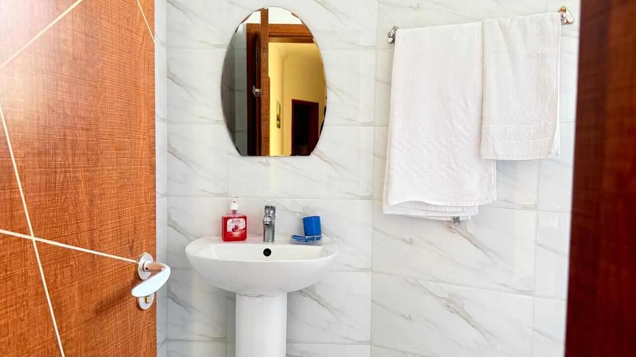 A bathroom with a white sink, a mirror, a towel rack with a white towel, and a wooden door.