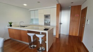 Una cocina moderna con una isla central, taburetes de bar, microondas y una puerta de salida de emergencia.
