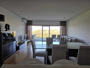 Un hotel moderno con mesa de vidrio, sofá, escritorio con computadora y un amplio ventanal corredera que da a un espacio exterior.