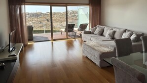Una sala de estar moderna con un sofá, sillas, una mesa de vidrio y vistas a un paisaje montañoso a través de amplios ventanales.