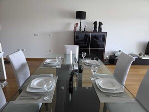 Un comedor con mesa de vidrio, sillas grises y lámpara negra.