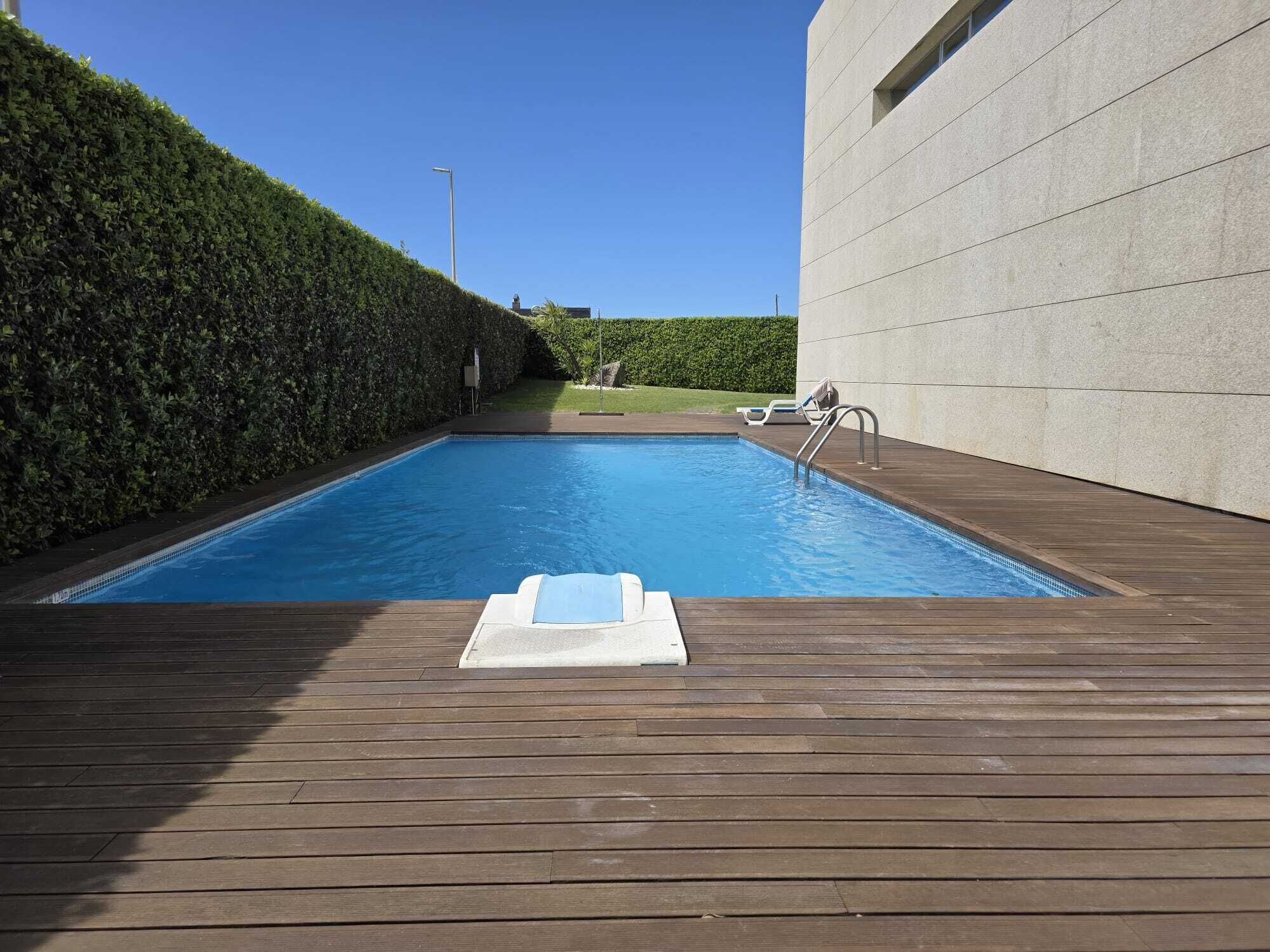 Una piscina con muelle de madera, una escalera metálica y seto.