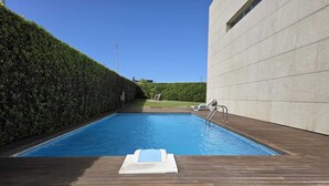 Una piscina con muelle de madera, una escalera metálica y seto.