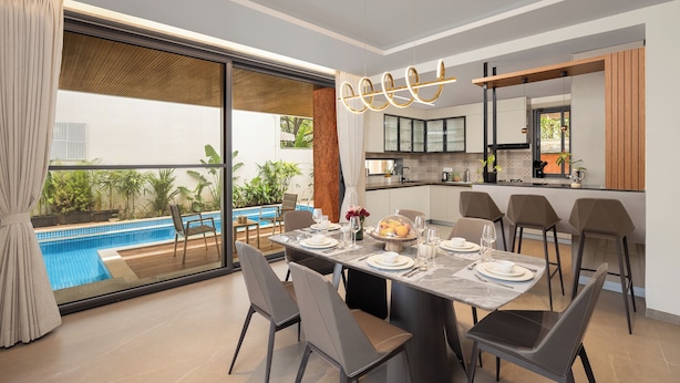 A modern dining area with a large table, chairs, and a view of a swimming pool. - Cloud 7 by ELIVAAS Luxurious 4 BHK Villa (Vagator)
