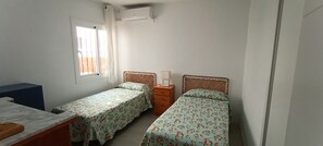 A room with two single beds, a small table, a dresser, and a window with curtains. - Beachfront Flat With Spectacular sea Views (Roquetas de Mar)