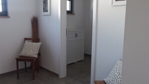 Una habitació àmplia amb un gran finestral, una cadira de fusta, un moqueta amb dibuixos i una cuineta al fons.