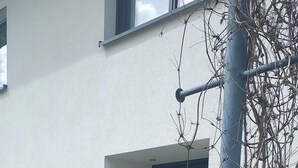 Edifici amb façana blanca, una porta i una finestra. Hi ha plantes en testos i un pal metàl·lic amb enfiladeres.