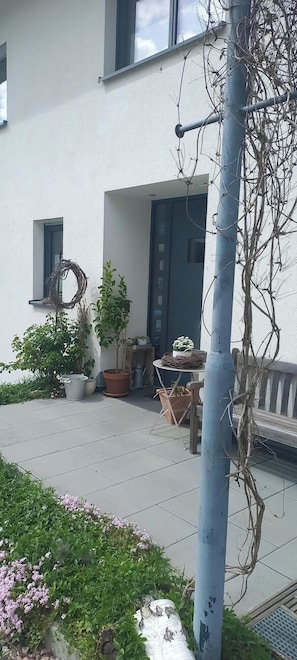A building with a white exterior, a door, and a window. There are potted plants and a metal pole with vines. - Rebgärtle vacation apartment in Markgräflerland (Müllheim im Markgräflerland)