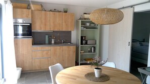 A modern kitchen with wooden cabinets, a built-in oven, and a dining area with a round table and chairs. - Rebgärtle vacation apartment in Markgräflerland (Müllheim im Markgräflerland)