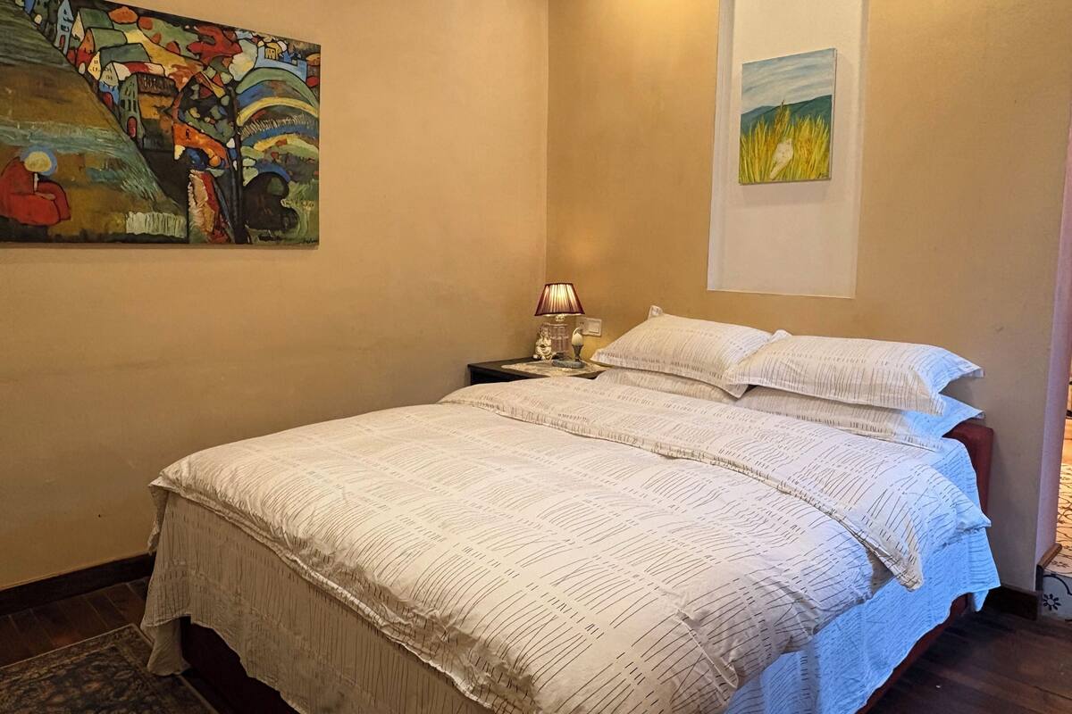 Une chambre à coucher avec un lit, une table de chevet, une lampe, un tableau et une photographie encadrée accrochée au mur.