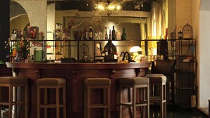 Een bar met houten krukken, flessenkasten en een kroonluchter.