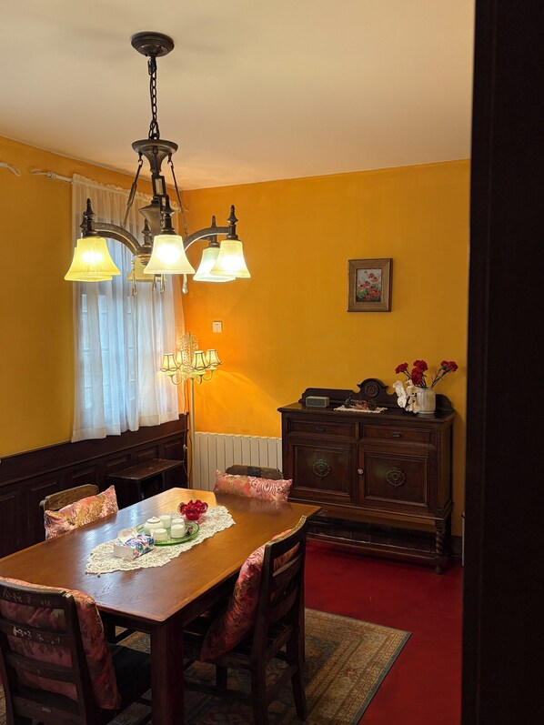 Comedor con mesa de madera, sillas, candelabro, radiador y aparador con flores.