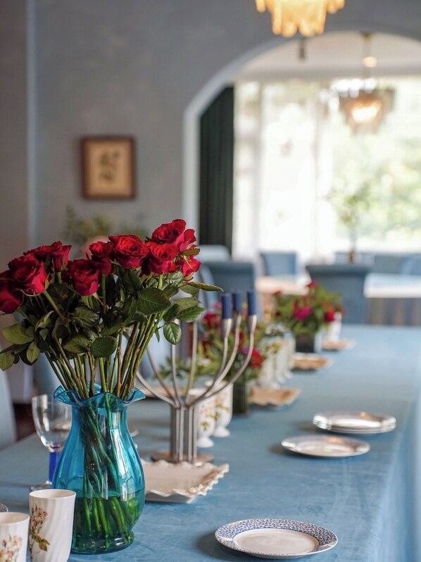 A long dining table with vases of red roses, candles, and plates set for a meal. - Lingdi Art Homestay in Moganshan (Huzhou)