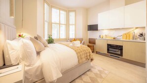 Ein modernes Schlafzimmer mit einem großen Bett, einem Nachttisch, einem Fernseher und einer Küchenzeile mit Herd und Schränken.