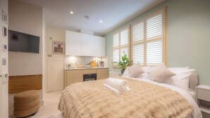A modern hotel room with a large bed, a small kitchenette, a TV, and a window with blinds. - Premium Studio 15 at The Orange Door Little Venice (Greater London)