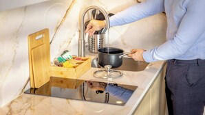 A person cooking at a kitchen with a marble countertop, a wooden cutting board, a pot, and a drawer with utensils. - Standard Studio 6 at The Orange Door Little Venice (Greater London)