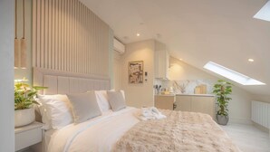 A modern bedroom with a large bed, a skylight, a potted plant, and a bedside table. - Premium Studio 14 at The Orange Door Little Venice (Greater London)