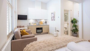 A modern hotel room with a sofa, a large bed, a kitchen area, and a TV. - Deluxe Studio 9 at The Orange Door Little Venice (Greater London)