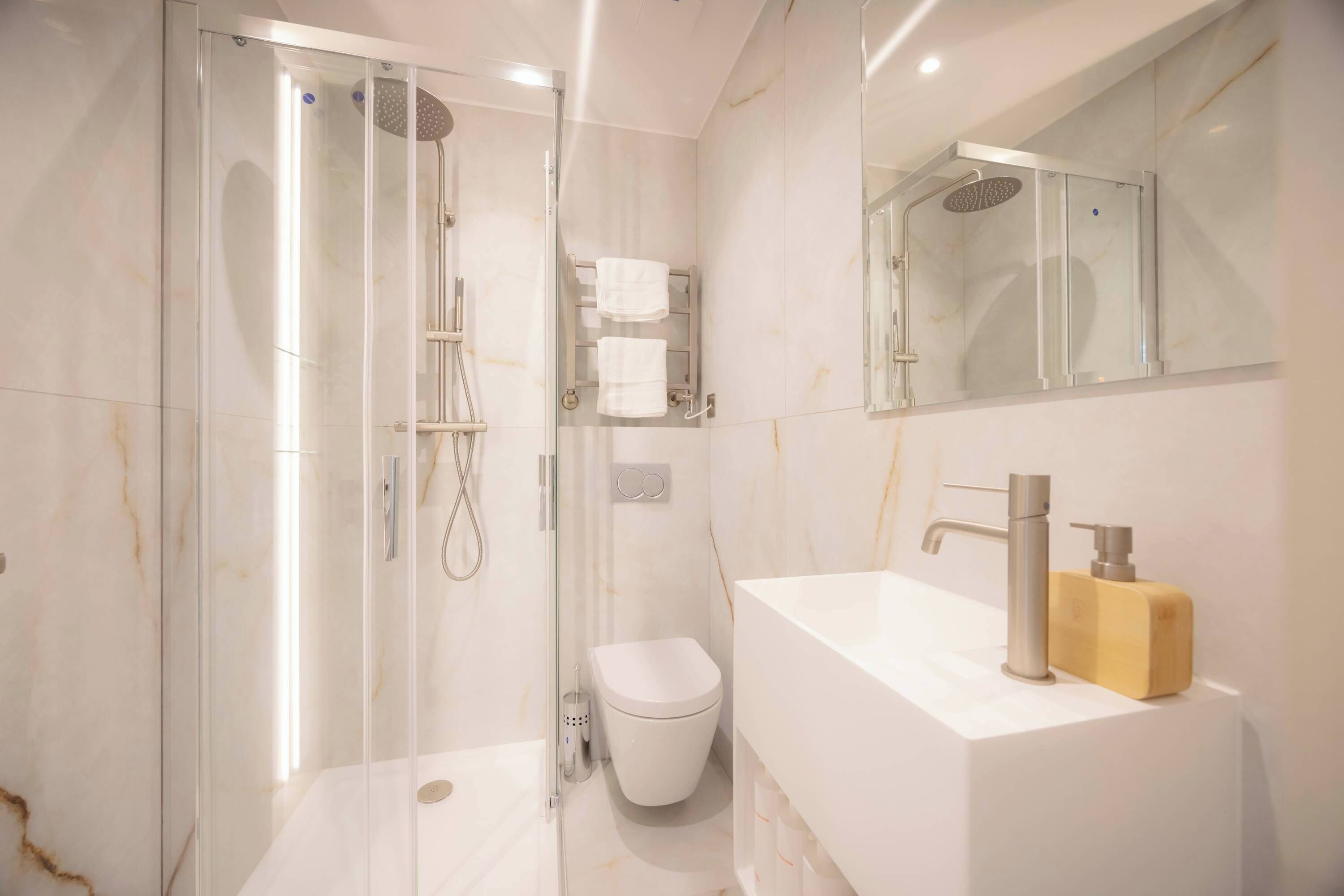 A modern bathroom with a glass-enclosed shower, a white sink with a wooden soap dispenser, and a toilet.