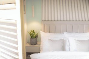 A bedroom with a bed, white pillows, a bedside table with a plant, and a headboard. - Premium Studio 12 at The Orange Door Little Venice (Greater London)