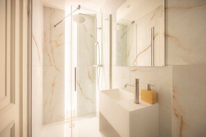 A modern bathroom with a glass-enclosed shower, a marble wall, and a white sink with a wooden soap dispenser. - Premium Studio 12 at The Orange Door Little Venice (Greater London)