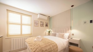Ein Schlafzimmer mit einem Bett, Nachttischen, einem Heizkörper, einem Fenster mit Jalousien und einer Wand-Klimaanlage.