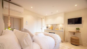 Un dormitorio moderno con una cama grande, una kitchenette pequeña, un televisor y una planta.